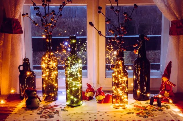 una mesa con cinco botellas de vidrio decoradas con guirnaldas de luces y flores secas decorativas
